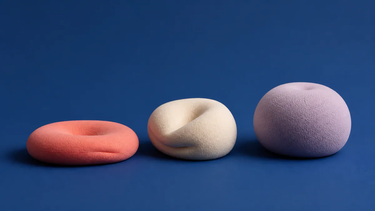 Coral, cream, and lavender rounded foam sculptures rest at different levels of compression on a cobalt studio surface.