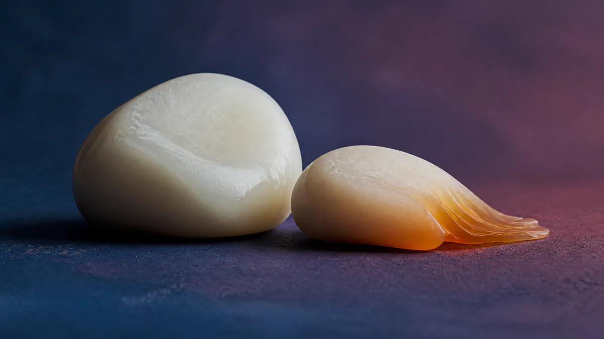 Two smooth wax forms rest together on a cobalt and plum surface, one melting into a warm amber ripple.