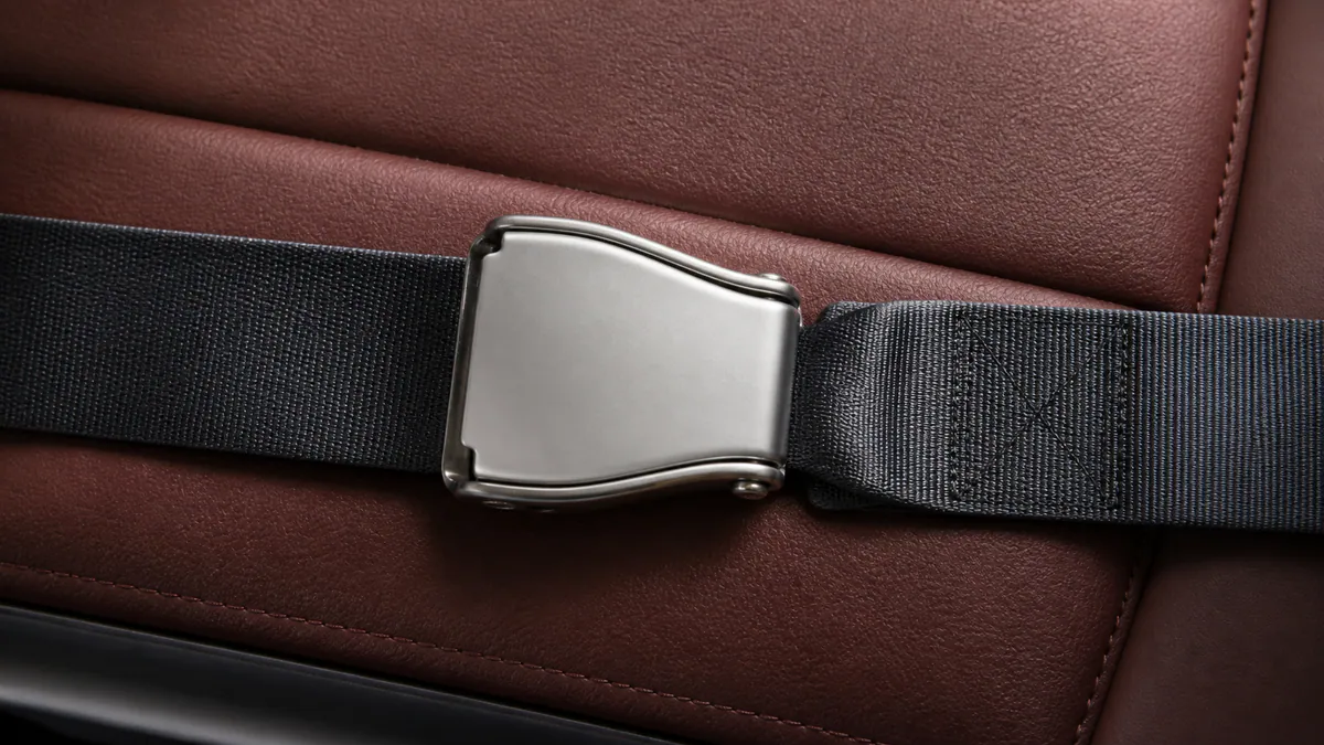 A fastened matte-metal aircraft lap belt lies across muted-russet seat upholstery.