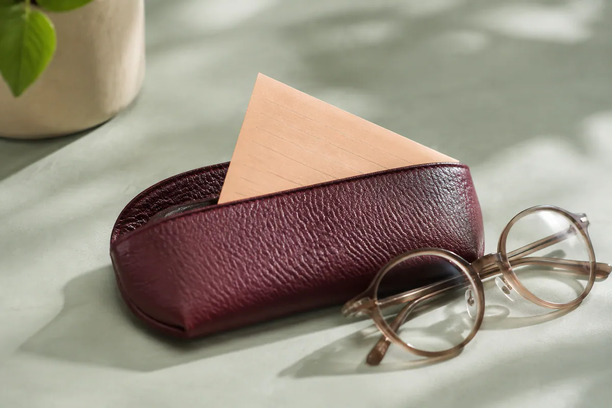 A blank apricot reminder card sits in a burgundy glasses case beside round spectacles on a mint tabletop.
