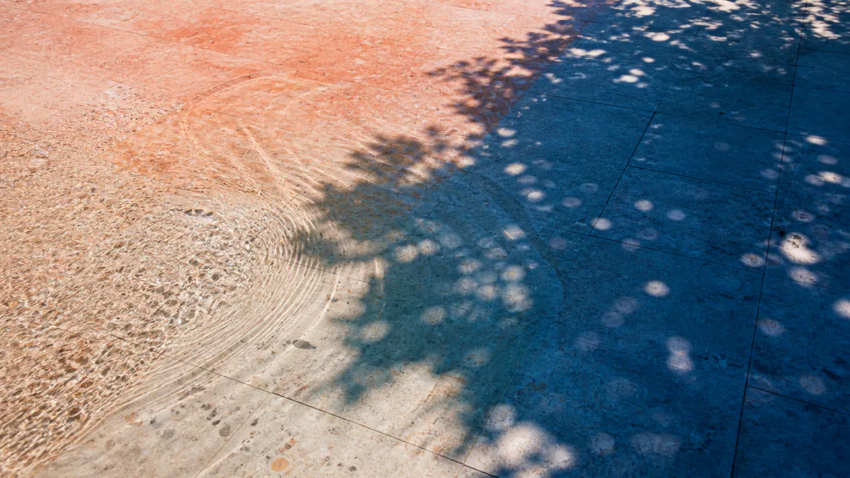 Clear water rippling across sun-warmed terrazzo into a pool of deep blue shade