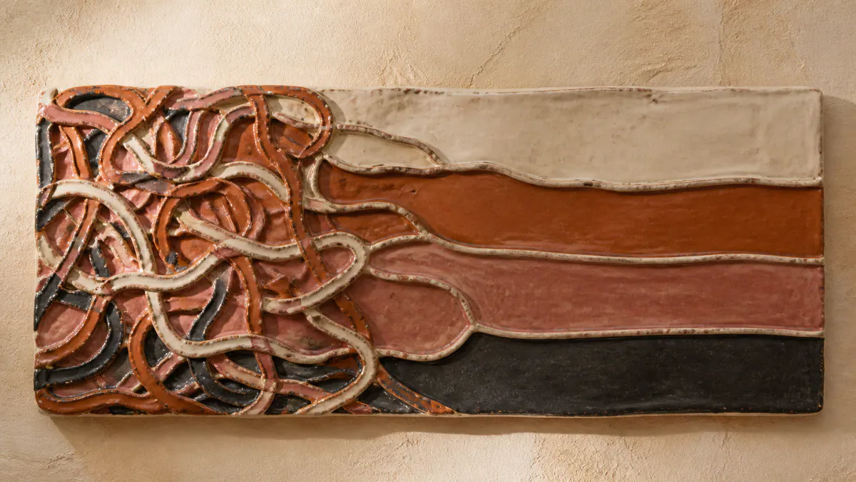 Wall-mounted ceramic relief with tangled warm-colored grooves opening into four broad bands.
