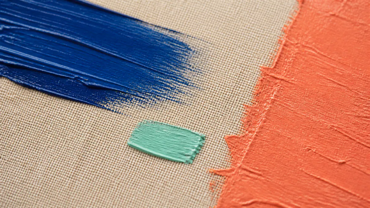 Thick ultramarine and coral brushstrokes frame a small mint paint swatch on raw beige canvas.