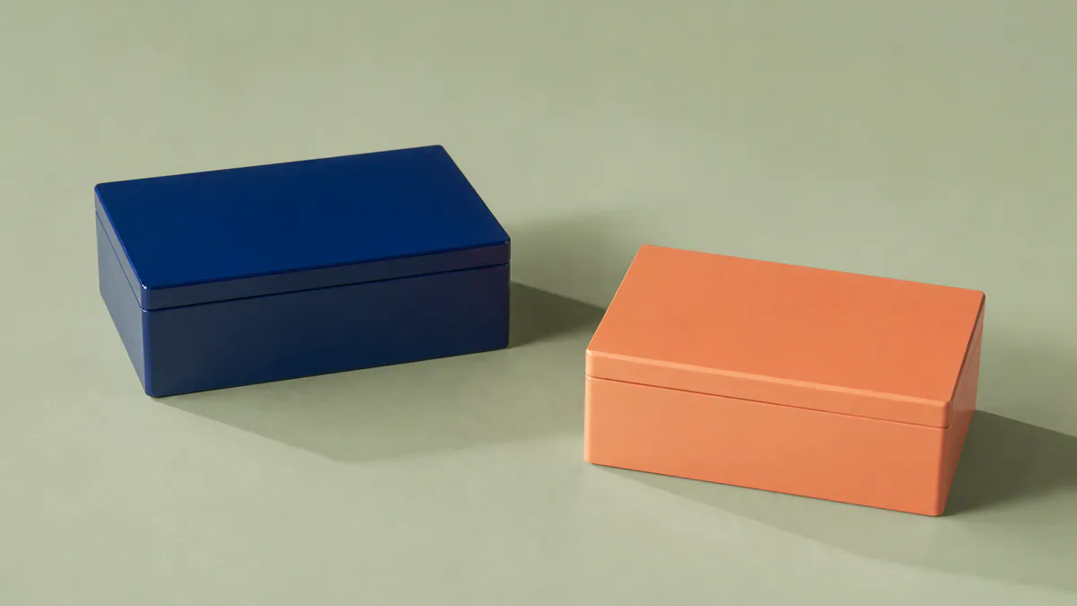 Two closed lacquered boxes, one cobalt and one apricot, rest on a pale-sage surface with their shadows overlapping.